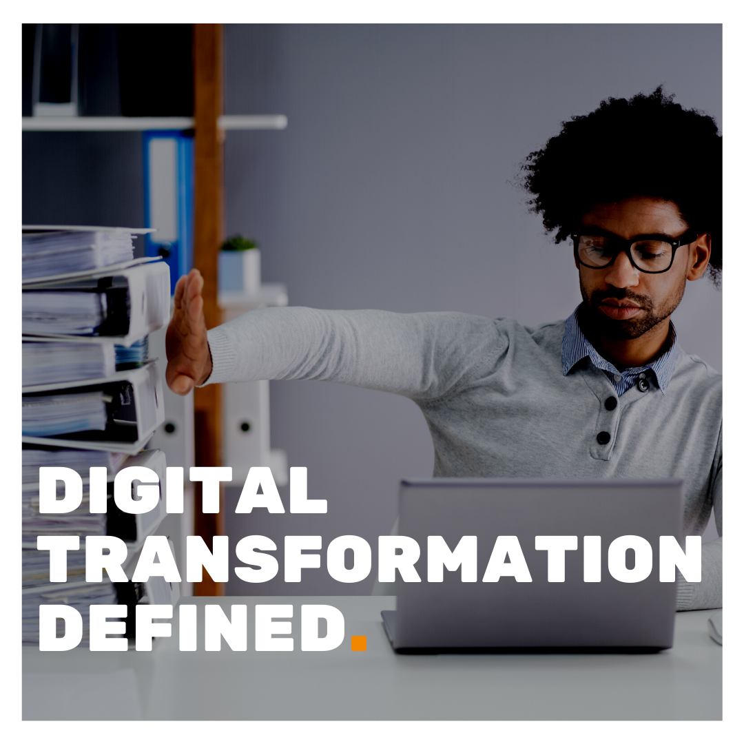 Digital Transformation Defined superimposed on a picture of a man using a laptop whilst pushing away a number of lever arch files