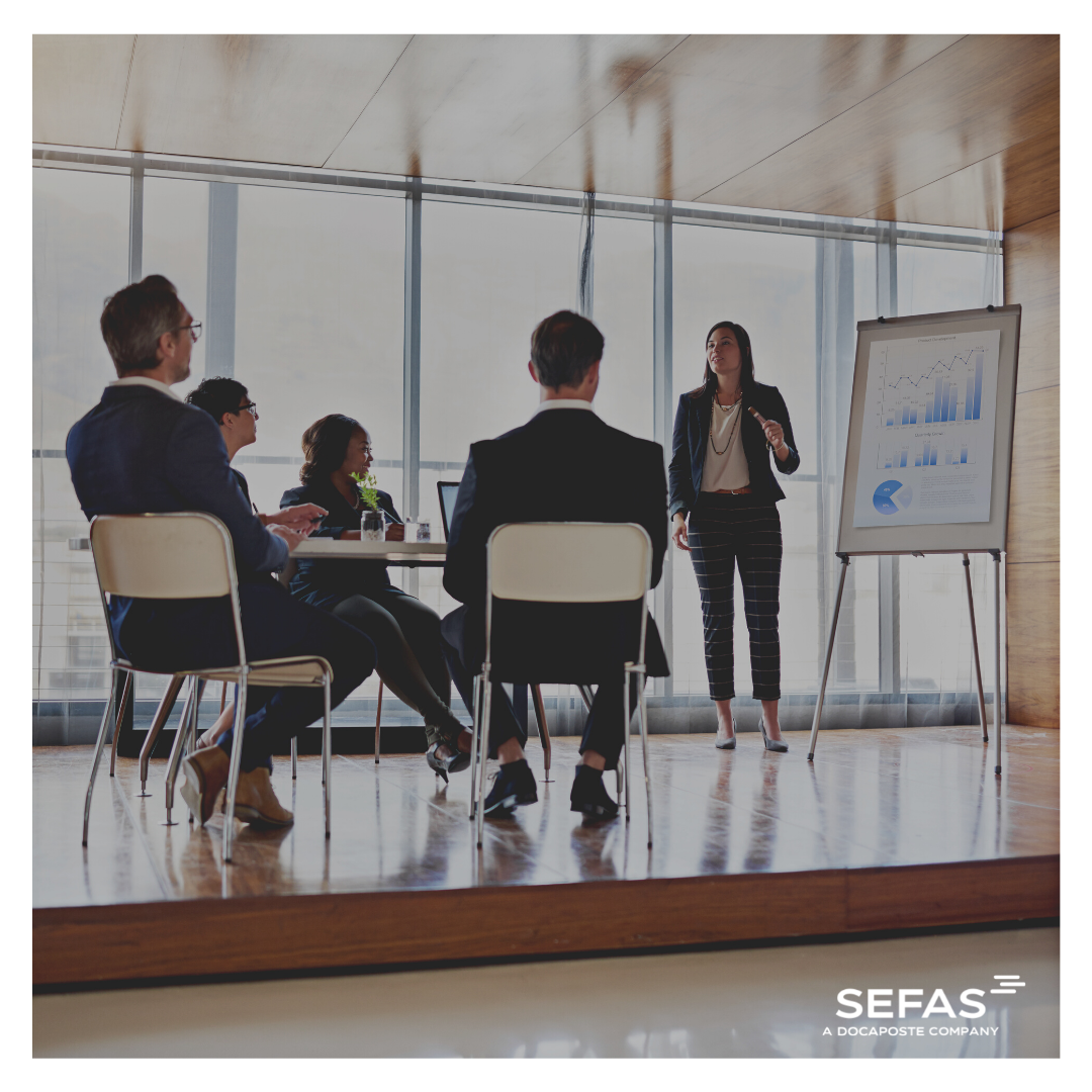 Training showing 4 people seating looking at a woman standing next to a whiteboard conducting training.