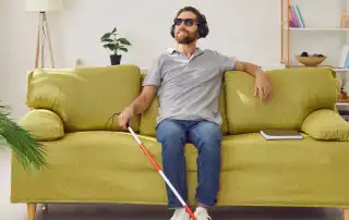Visually impaired man with cane sitting on couch and listening to music through headphones