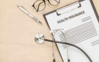 a clipboard with a stethoscope, a pen, and some glasses sat on a wooden table