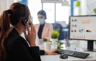Customer service representative wearing a headset, working on a computer with data charts on the screen in a modern office.
